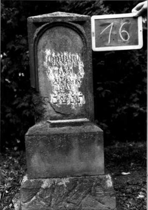 Grabstein 16 (Index: 100110419) Material: Sandstein Zustand: stark verwittert und beschädigt mit großem Textverlust Maße HxBxT: 105x40x23 cm Beschreibung: Stele, getreppter Sockel, unterer Sockel rusticaartig, obeliskenartiger Abschluß, Schriftfeld eingetieft mit Rundbogen: Grabstein 16