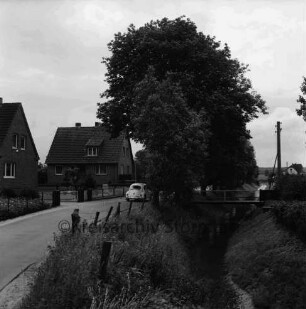 Ölmühle: rechts Barnitz mit Fußgängerstegen: links Einfamilienhäuser: in der Mitte Bäume und VW Käfer: hinten rechts Strommast und Wohnhaus: 3. Juli 1971