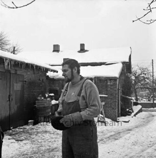 Bildhauer Rolf Goerler vor der alten Schmiede: Ausbau zum Atelier: hinten Holzböcke und Kisten: Winter