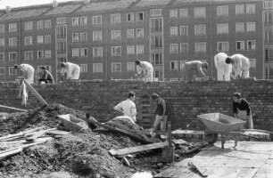 Baustelle vor einem bereits bewohnten Wohnblock. Maurer beim Hochziehen einer Ziegelwand