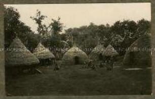 Afrikaner auf einem Platz zwischen Kraalhütten