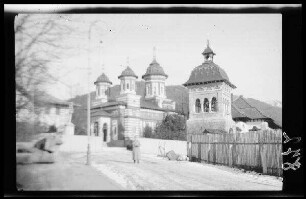 Kirche in romanischem Stil mit drei Türmen und gestreiftem Mauerwerk und kleinem Glockenturm (?) im Vordergrund