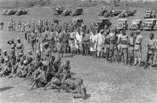 Maskalfest in Gonder : Italienische Kolonialsoldaten auf dem Maskalfest in Gonder. Im Hintergrund einige Automobile und Lastwagen die als Tribüne genutzt wurden. Im Vordergrund äthiopische Jugendliche der faschistischen Jugendorganisation Balilla.