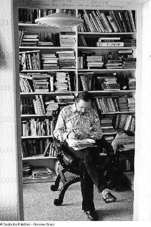 Der Schriftsteller Heinz Czechowski schreibend vor einem Bücherregal sitzend, aufgenommen in seiner Wohnung in Halle-Neustadt