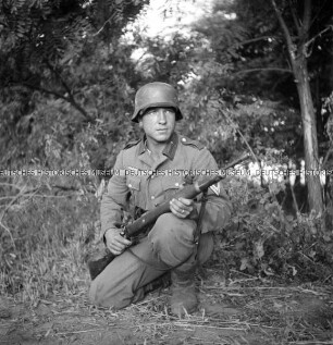 Hermann Hirchenhein kniet in Uniform und mit Gewehr in einem Wald