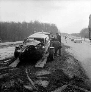 A1: Verkehrsunfall: mit Pkw-Kombi und Tanklastzug: Unfall-Kombi mit eingedrückter Front auf Plattform von Abschleppwagen: daneben Fahrer von Abschleppwagen, Mann bückt sich: Fahrbahn abgestreut: hinten Polizist beim Leiten des Verkehrs, Leitkegel, vorbeifahrende Autos: hinten Bäume