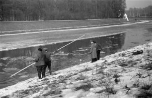 Zugefrorener Elsterflusslauf : Zwei Männer mit Stangen beim Abfischen von durch Eissprengungen getöteten Fischen am zugefrorenen Elsterflusslauf.