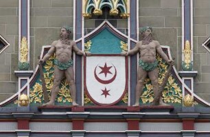 Stadtwappen, von zwei Figuren im Wilhelminischen Stil flankiert