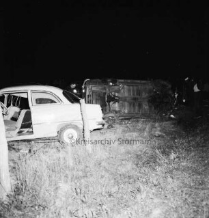 B 404: bei Tralau: Verkehrsunfall: auf Kreuzung mit Landstraße zwischen Tralau und Bad Oldesloe: Zusammenstoß von zwei Pkws: beide Unfallwagen auf Wiese, einer davon auf Seite liegend: zwei Männer, Polizist: davor Weidezaun: im Dunkeln, 15. Oktober 1959