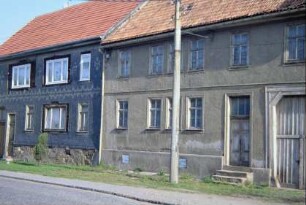 zwei Bauernhäuser an der Hauptstraße; jeweils Haustür zur Straße und überbaute Torfahrten