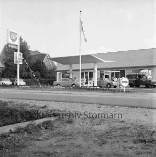 BP-Tankstelle: Hamburger Straße: Neubau: rechts Gebäude: davor Zapfsäulen mit tankenden Pkws, Kleintransporter und Personen: links BP-Schild und parkende Pkws: dahinter Bäume und Wohnhäuser