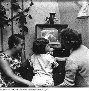 Zwei Frauen mit Kind vor laufendem Fernsehgerät sitzend