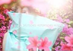 Sphärische Stimmung im Gegenlicht: Junge Frau in hellblauer Plastikkleidung mit aufgeklebten Blüten zwischen Rhododendren (Prämiertes Foto Sonderthema: Wunderland) (Altersgruppe S)