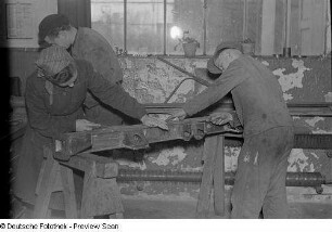 Lehrlinge mit Meister beim Bearbeiten eines Metallteils