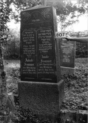 Grabstein 807 (Index: 99802331) Material: Granit, poliert Zustand: sehr gut Maße HxBxT: 225x71x28 cm Beschreibung: Sockel, obeliskartige Stele Symbolik: Davidstern, Palmzweige, Inschriftenfeld in stilisierter Form der Gesetzestafeln Besonderheit: Endreim: Grabstein 807