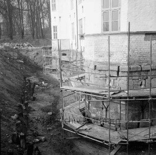 Restaurierung: innerer Graben ausgehoben: Pfosten der früheren Grabenversteifung mit Holzbohlen am Grabenfuß: Gerüst an Schlossfundament