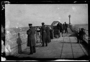 [Zeebrugge (Belgien)]: Offizier und Matrosen bei Fernrohren und einem Geschütz auf einer Mole, im Hintergrund ein Leuchtturm ("am Geschütz in (?)")
