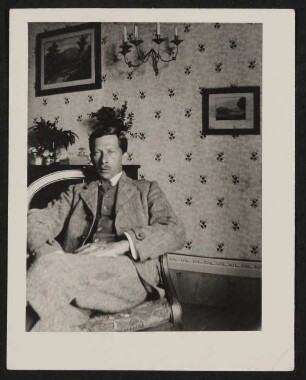 Rudolf Borchardt sitzt mit überschlagenen Beinen in einem Sessel