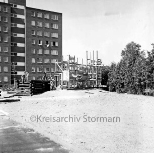 Kinderspielplatz mit spielenden Kindern: rechts Baumreihe: hinten links Wohnblock