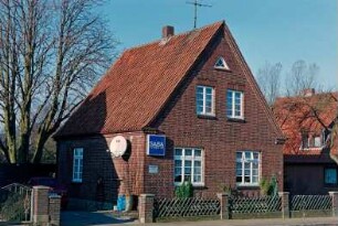Dorfstraße 3: giebelständiges Kleinsiedlungshaus aus Backstein: Straßenfront mit Sprossenfenstern, Werbeschild: Traufseite: davor Jägerzaun, Hofeinfahrt