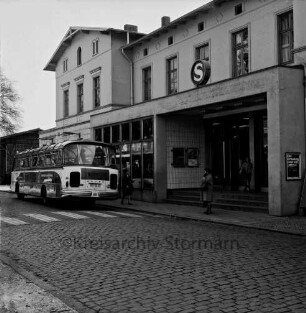 Bahnhofsgebäude: Straßenfront: Teilansicht mit Eingang: wartender Reisebus