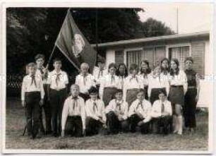 Gruppenbild von Thälmann-Pionieren mit Fahne vor einem Bungalow im Pionierlager