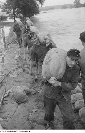 Männer bei Schutzvorkehrungen (Stabilisieren eines Dammes mit Hilfe von Sandsäcken)