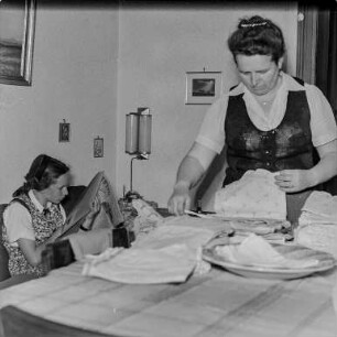 Mutti und Christel : Portrait der Ehefrau des Fotografen, Helene Heine, bei der Hausarbeit. Links lesend Tochter Christel