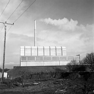 Blick auf den Müllbunker und den Schornstein: vorn Baugrube, Strommast und Büsche