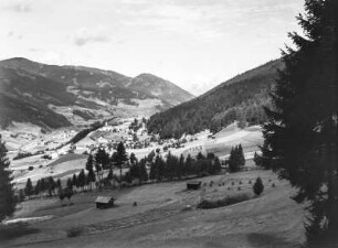 Dorf im Tal : Blick in ein Tal mit Hütten am Hang und einem Dorf im Hintergrund