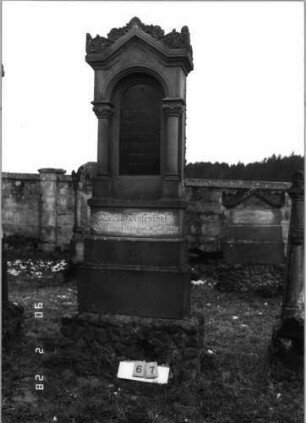 Grabstein 67 (Index: 100114875) Material: Sandstein und polierter Granit Zustand: leicht verwittert im Giebel Maße HxBxT: 262x66x29 cm Beschreibung: Ädikula mit gestuftem Sockel auf Rustikasockel, eingezogener Spitzgiebel mit Akroteren und Voluten, eingesetzte Texttafel: Grabstein 67