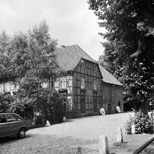 Trittauer Wassermühle: davor Weg mit Kopfsteinpflaster: vorn rechts Begrenzungssteine: links Heck eines Pkws: hinten rechts und links Bäume