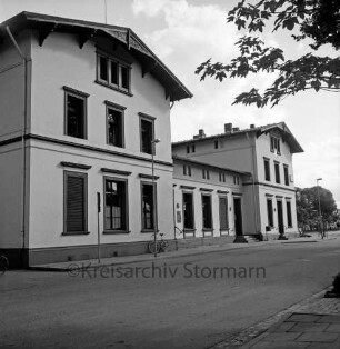 Bahnhofsgebäude: Straßenfront: davor Straßenlampen, Briefkasten, Verkehrsschild, angelehntes Fahrrad: vorne Bahnhofstraße, Bürgersteig
