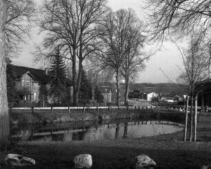 Dorfteich: davor Grünanlage mit Feldsteinen, Blumenrabatten und Bäumen: hinten Heilsaustraße: dahinter Häuser und Gärten