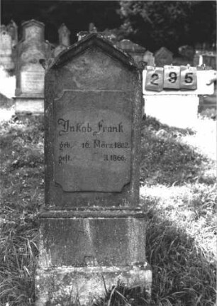 Grabstein 295 (Index: 100106865) Material: Sandstein Zustand: stark verwittert, teilweise Textverlust, Mittelaufsatz fehlt Maße HxBxT: 139x50x17 cm Beschreibung: Stele, eingezogener Giebel mit Verdachung, Mittelaufsatz fehlt, Schriftfeld plakettenförmig erhaben, getreppter Sockel: Grabstein 295