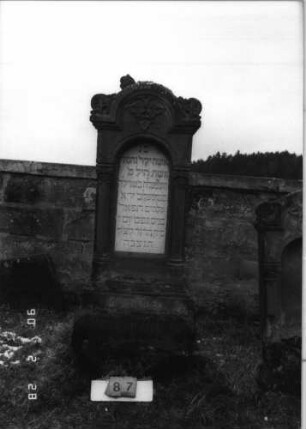 Grabstein 87 (Index: 100114834) Material: Sandstein und ? Zustand: Stele und Giebel beschädigt, leicht verwittert Maße HxBxT: 180x61x30 cm Beschreibung: Ädikula, Blatt im Giebel: Grabstein 87