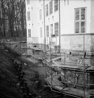 Restaurierung: innerer Graben ausgehoben: Pfosten der früheren Grabenversteifung mit Holzbohlen am Grabenfuß: Gerüst an Schlossfundament