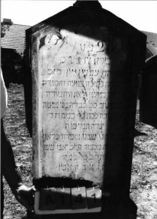 Grabstein 141 (Index: 99798051) Material: Sandstein, weiß Zustand: leicht verwittert Maße HxBxT: 147x52x17 cm Beschreibung: Stele, giebelartiger Abschluß, getreppter Sockel Symbolik: Rundbogenfries: Grabstein 141A