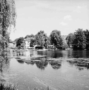 Mühlenteich: Blick von Süden Am Mühlenteich auf gegenüberliegendes Ufer: hinten Mitte zwischen Bäumen Elektriziätswerk Reinbek-Wentorf GmbH [später: e-werk Sachsenwald]: hinten rechts Schloss Reinbek: hinten links Brücke der Schlossstraße über Bille: dahinter Gebäude: vorn links Baum