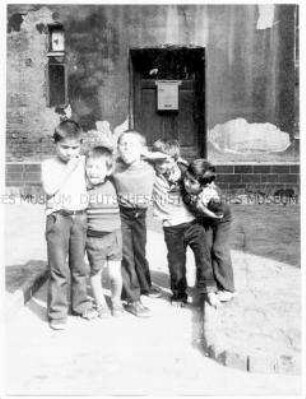 Fünf kleine Jungen, die Arme umeinander gelegt, auf einem Hinterhof (Altersgruppe bis 14)