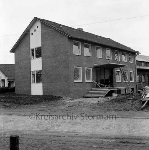 Amtsverwaltung: Hauptstraße: Amtshaus vor Fertigstellung: im Vordergrund Zaun: vorn unbefestigte Außenanlagen: rechts Außentreppe: darauf und daneben Baumaterial: dahinter Leiter an Wand: hinten rechts ehemalige Volksschule