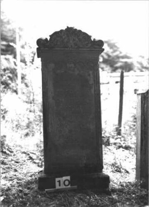 Grabstein 10 (Index: 99898700) Material: Sandstein Zustand: stark verwittert Maße HxBxT: 155x55x27 cm Beschreibung: aufgesockelte hochrechteckige Stele, Aufsatz mit Akanthusornamenten, über dem Schriftfeld Rundbogenfries Symbolik: Akanthus, Rundbogenfries: Grabstein 10
