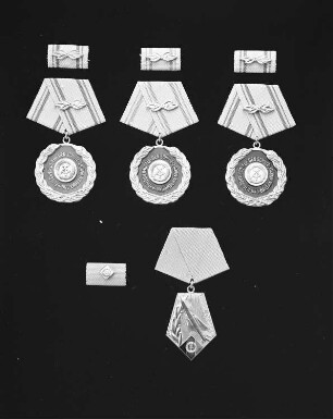 Auszeichnungen der Nationalen Volksarmee. Oben: 3 Medaillen zum Ehrentitel "Verdienter Angehöriger der NVA" an blauer Bandspange (Buntmetall, goldfarben rot bzw. grün emailliert; Durchmesser ca. 35 mm, Gewicht 34,46 g (mit Spange); gestiftet 1975). Avers mit Staatswappen, Lorbeerkranz und Inschrift. Unten links: Interimsspange mit Staatsemblem. Unten rechts: Medaille zum Ehrentitel "Verdienter Militärflieger der Deutschen Demokratischen Republik" an blauer Bandspange (fünfeckig, Buntmetall, goldfarben, emailliert; 41,5 x 31,5 mm; 1976/1989, gestiftet 1974). Avers mit Staatsemblem, Lorbeerzweig und Abfangjäger vom Typ MIG