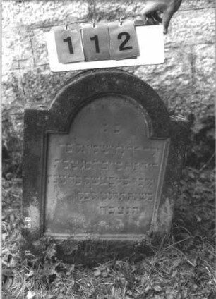 Grabstein 112 (Index: 99609748) Material: Sandstein Zustand: verwittert Maße HxBxT: 71x53x9 cm Beschreibung: Stele, eingezogener Rundbogenabschluß, Schriftfeld eingetieft Besonderheit: Kindergrab: Grabstein 112