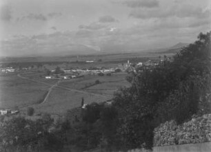 Landschaftsblick : Eine weite Landschaft mit landwirtschaftlich genutzten Flächen. Im Zentrum eine Siedlung.