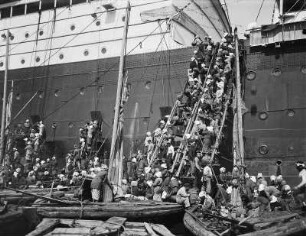 Nagasaki (Japan). Hochseepassagierdampfer "Cleveland" beim Kohlebunkern. Einheimische Arbeiterinnen und Arbeiter transportieren Kohle in Körben aus Dschunken über provisorische Fallreeps zu Ladeluken und an Bord
