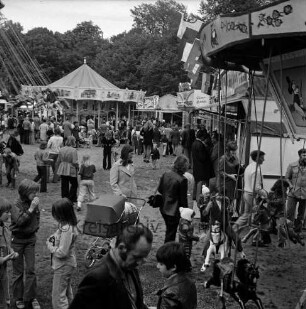 Frühjahrsmarkt: Volksfest: Exer: links Jugendliche auf Kettenkarussell: vorn rechts und hinten links Kinderkarussells mit Kleinkindern: dazwischen Besucher: hinten links Jahrmarktsbuden: hinten Mitte Bäume