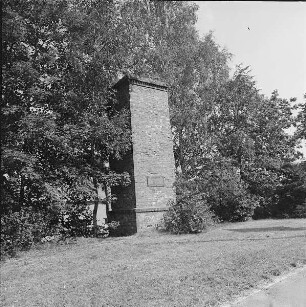 Rodewisch, Lengenfelder Straße. Schornsteinstumpf eines ehemaligen Messingwerkes (Ziegelstein; um 1860), Ansicht mit Gedenktafel (signiert und datiert K. Schott 1962) mit Inschrift "Der Essenstumpf ist der letzte Rest der Messingbrennhütte. 1603-1924 stand hier das Messingwerk Niederauerbach"