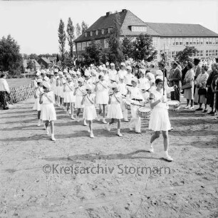 Kindervogelschießen: Umzug: vor Matthias-Claudius-Schule: Spielmannszug der "Old Reinfelder Jungs": Zuschauer, Jägerzaun: im Hintergrund Häuser der Ahrensböker Straße, 27. Juni 1964