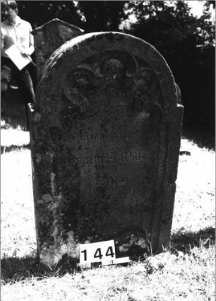 Grabstein 144 (Index: 100085461) Maße HxBxT: 104x60x16 cm Beschreibung: Stele, eingezog. Rundbogenabschl. , Schriftfeld eingetieft mit Maßwerk auf Vordersei: Grabstein 144